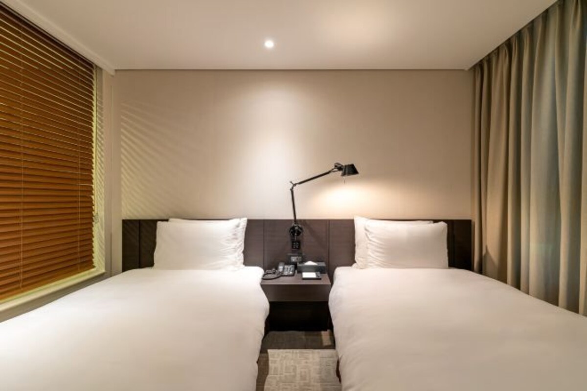 Ein Hotelzimmer mit zwei Betten, einem Nachttisch, einer Lampe und einem Fenster mit Jalousien.