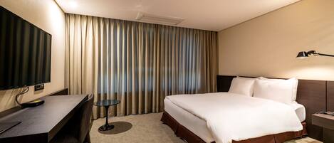 Habitación de hotel con cama, escritorio, silla, televisor y lámpara.