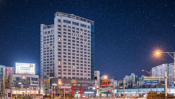 A nighttime cityscape with a prominent high-rise building, illuminated signage, and a roundabout with traffic. - THE SKY HOTEL (Cheonan)