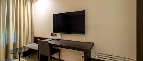Habitación de hotel con un escritorio de madera oscura, un televisor de pantalla plana en la pared, una mesita redonda pequeña, una silla y una cama con cabecera.