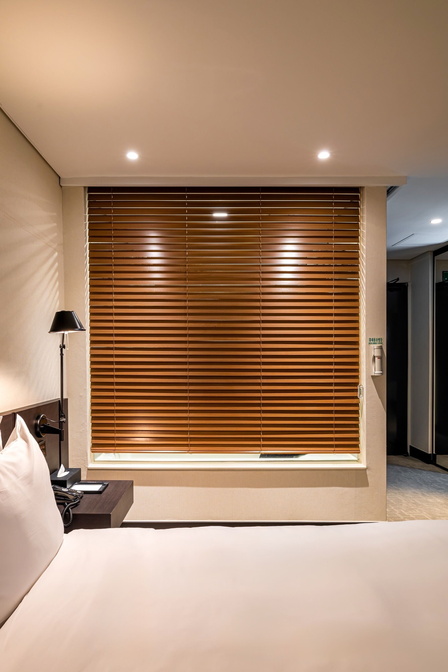 Habitación de hotel con una cama grande, una lámpara de noche, una mesita de noche y una ventana con persianas.