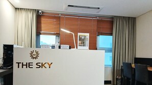 A reception desk with "THE SKY" logo, a computer, and a window with blinds. - THE SKY HOTEL (Cheonan)