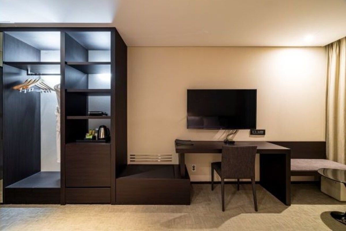 Ein kleines Hotelzimmer mit Bett, Schreibtisch, Stuhl, Fernseher und einem Kleiderschrank mit Einlegeböden.