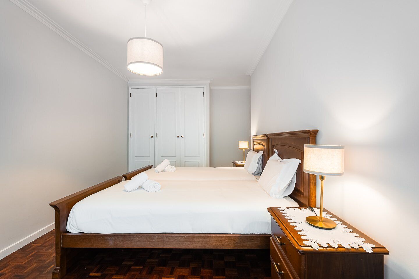 A neatly arranged hotel room with a large bed, a wooden nightstand, a bedside lamp, and a wardrobe.