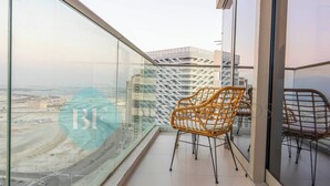 A balcony with a wicker chair, glass walls, and a view of a cityscape with buildings and construction.