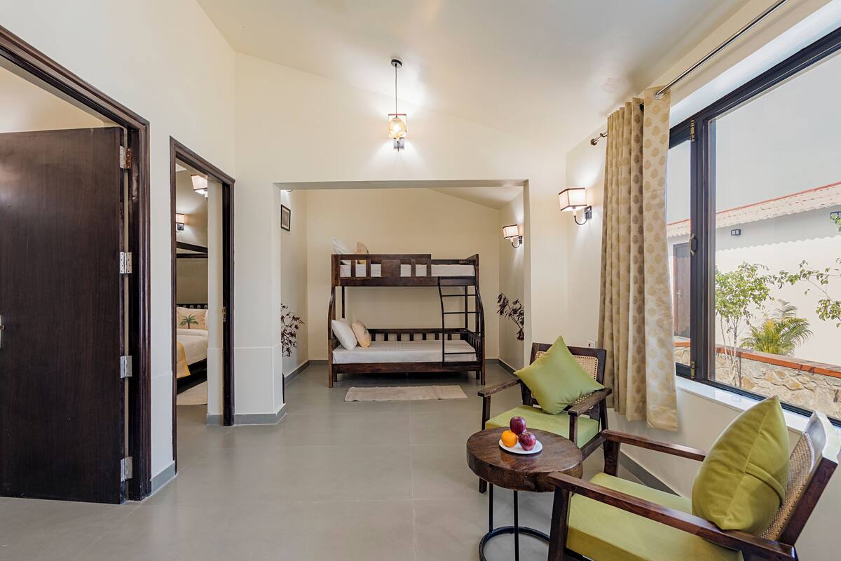 Une chambre avec un lit superposé, une petite table avec des fruits, une chaise et une fenêtre avec des rideaux.