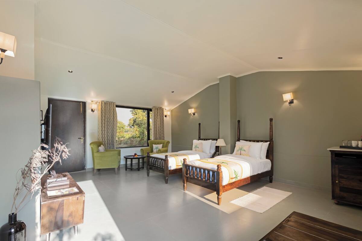 Une chambre avec deux lits, un fauteuil vert, une petite table et une armoire en bois.