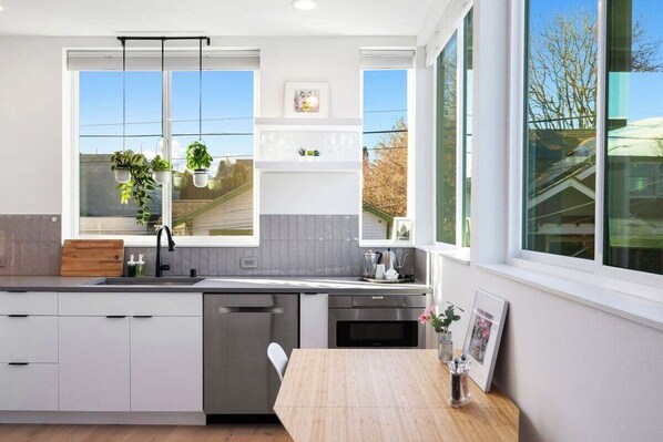 A modern kitchen with a large window, white cabinetry, and a wooden countertop.