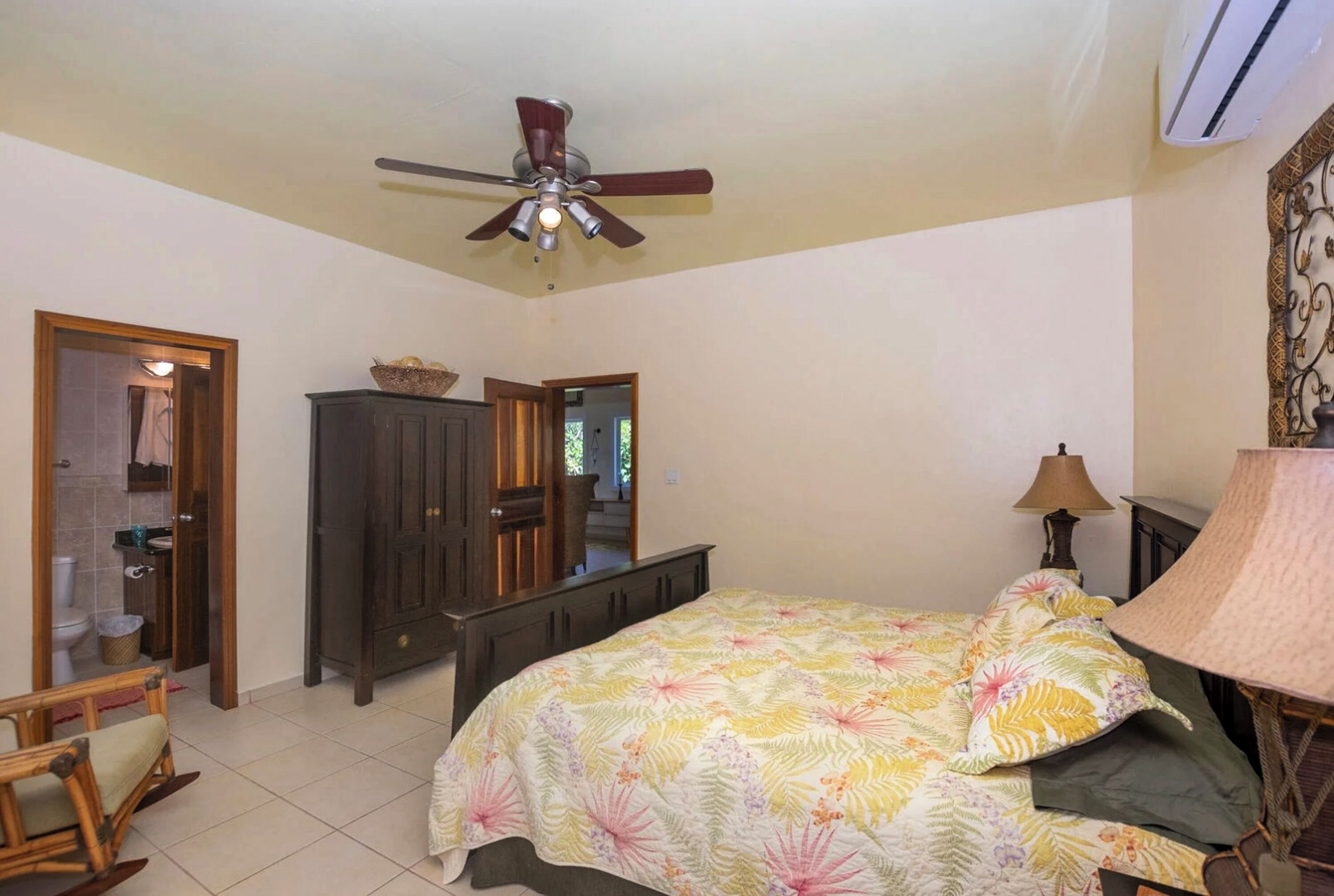 A bedroom with a bed, a ceiling fan, a dresser, and a lamp.