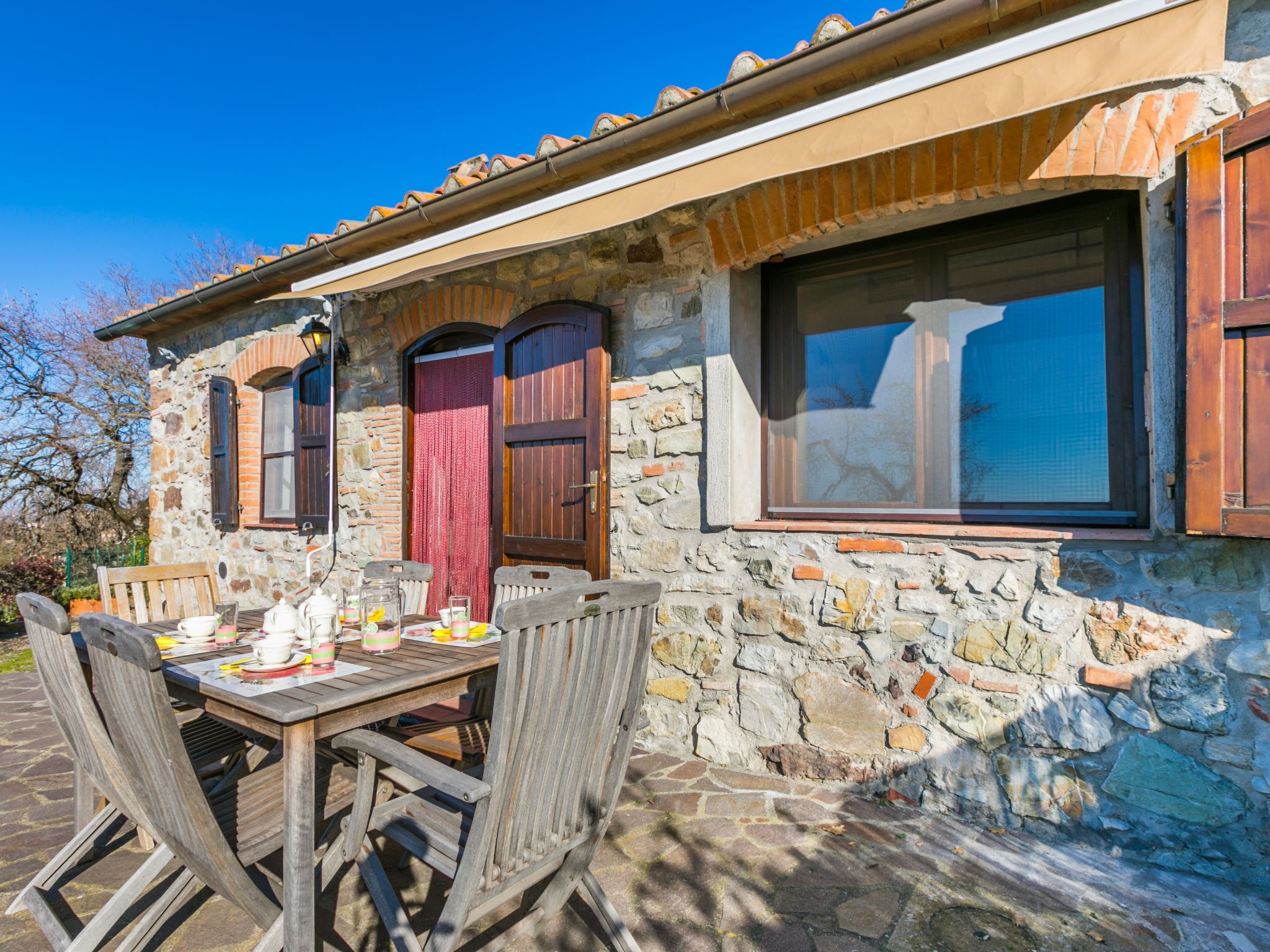 A stone building with a tiled roof, wooden shutters, and a table set for dining.