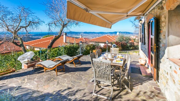 Une terrasse avec une table et des chaises, un parasol et une vue sur une ville aux bâtiments aux toits rouges.