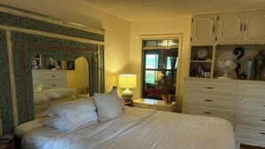 Un letto rifatto con lenzuola bianche, una lampada da comodino, un comò con cassetti e uno specchio con decorazioni elaborate.