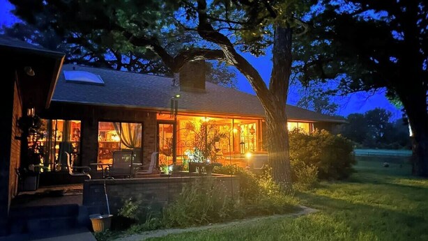 Una casa con un portico ben illuminato, un albero grande e un prato.