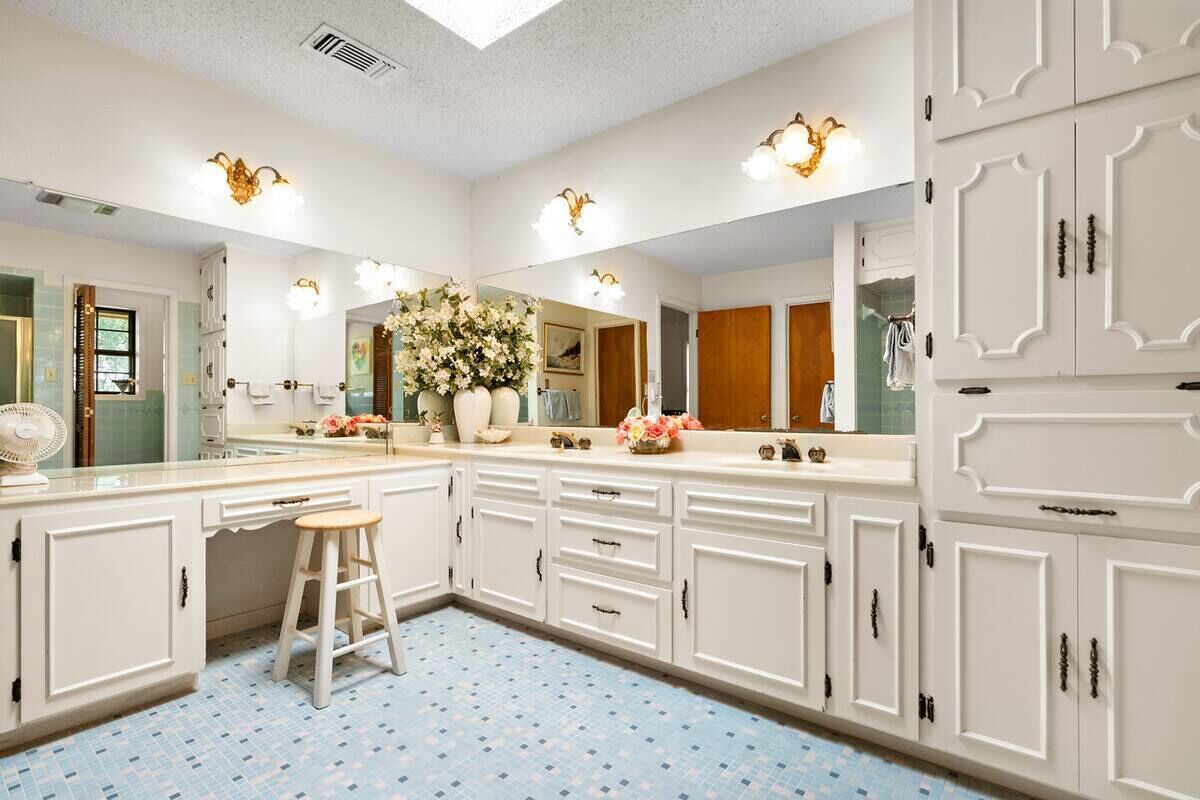 Una cocina amplia con armarios blancos, una isla central con un taburete y un espejo grande sobre la encimera.