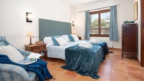 A hotel room with a bed, a chair, a nightstand, a dresser, a window with curtains, and a view of the outdoors. - Charming finca with large pool and garden in Santanyi for up to 8 persons (Santanyi)