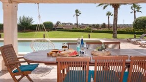 A covered outdoor dining area with a pool view, wooden furniture, and a hanging chair. - Incredible finca with huge garden and pool for up to 8 persons in Santanyi (Santanyi)