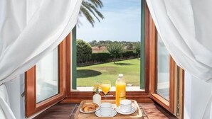 A breakfast setup with croissants, coffee cups, and orange juice on a wooden tray by a window with a view of a golf course. - Incredible finca with huge garden and pool for up to 8 persons in Santanyi (Santanyi)