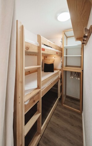 A bunk bed room with a wooden frame, a small shelf, and a mirror.