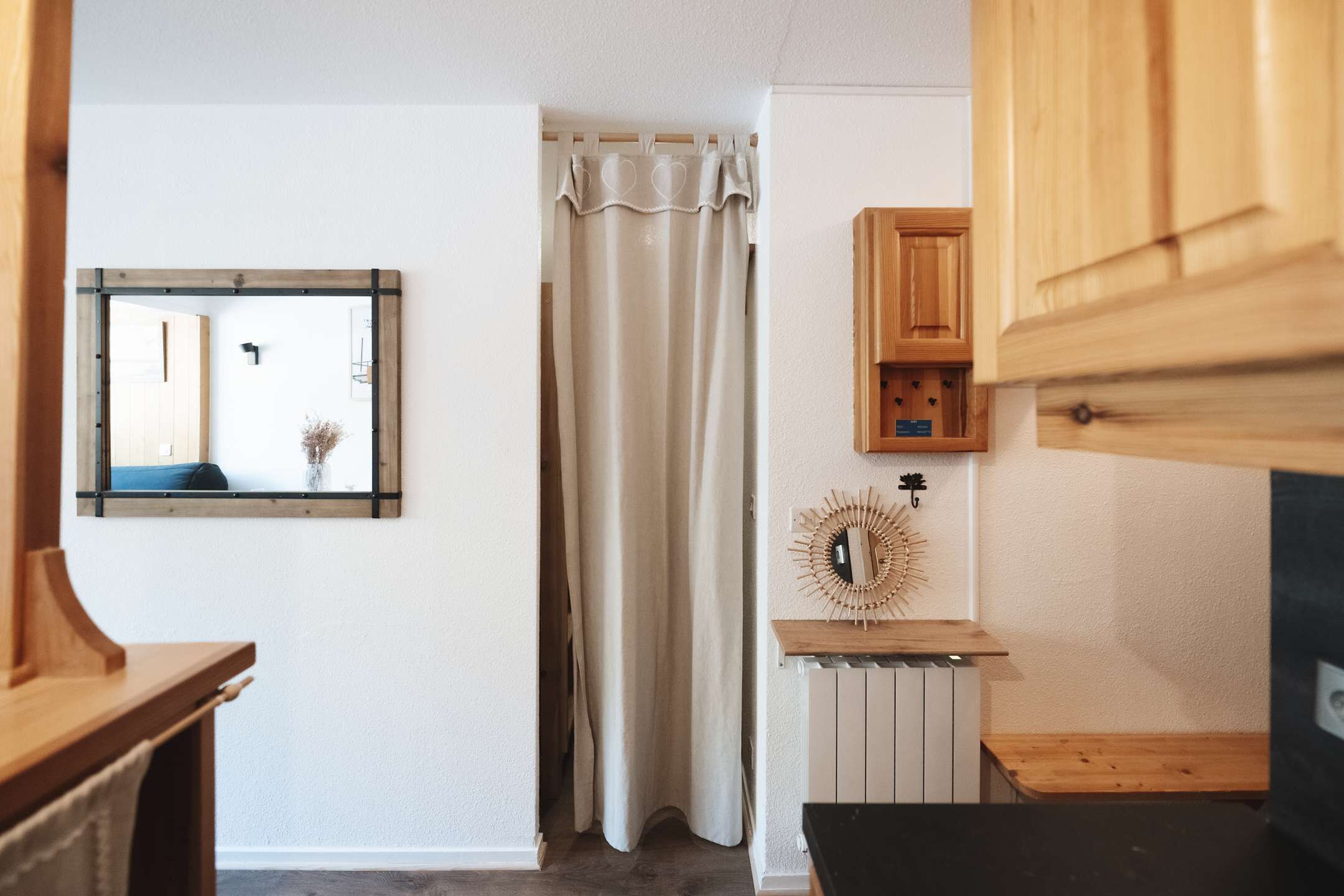 Een kamer met een houten kast, een spiegel, een gordijn en een decoratief object op een plank.