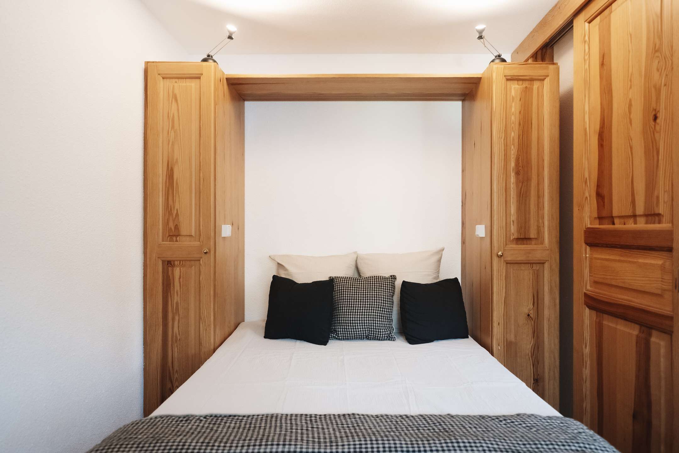 Een slaapkamer met een bed, kussens en houten garderobedeuren.