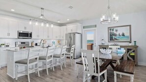 Una cocina moderna con armarios blancos, un refrigerador de acero inoxidable y un comedor con sillas blancas y una mesa de madera.