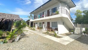 A two-story building with a balcony, a thatched-roof structure, and potted plants. - Coconut Inn (Moalboal)