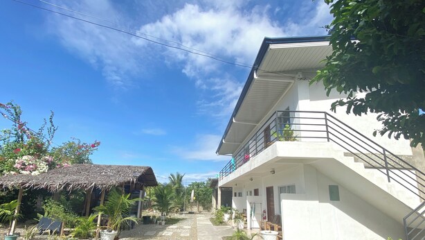 A two-story building with a balcony, surrounded by potted plants and a gravel path. - Coconut Inn (Moalboal)
