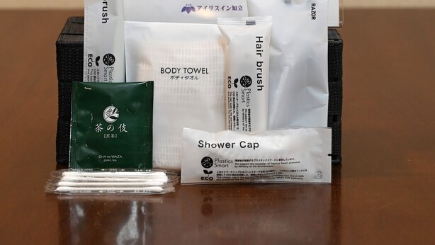 A promotional display for Amenity Corner with various toiletries including a toothbrush, body towel, hair brush, and shower cap. - Iris in Chiryu (Chiryu)