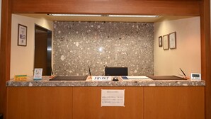 Una recepción con mostrador de granito, un reloj digital y un cartel que indica la zona de recepción.