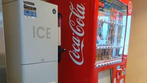 Máquina expendedora con el logotipo de Coca-Cola y un dispensador de hielo contiguo.