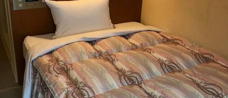 A hotel room with a bed, a bedside table, a wall clock, and a light fixture.