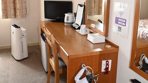 Habitación de hotel con escritorio de madera, televisión de pantalla plana, espejo, hervidor blanco y estación de carga.