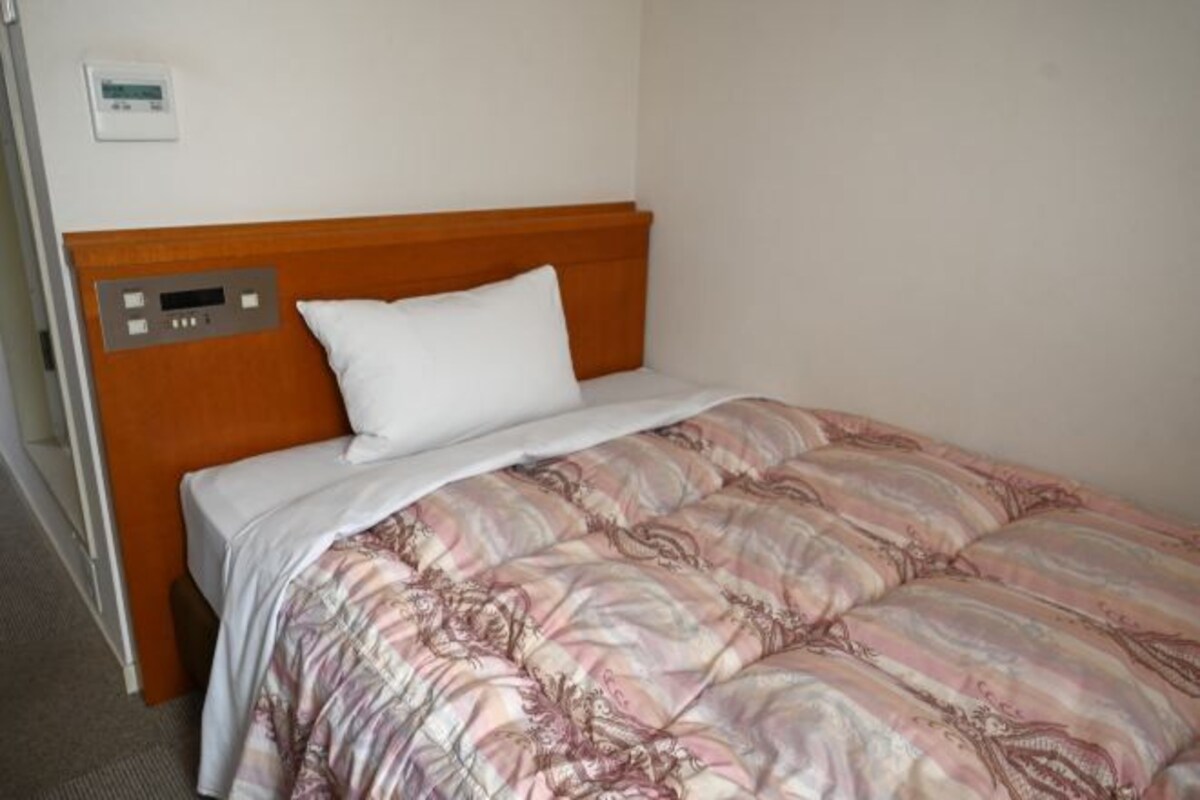 Una cama individual con cabecera de madera, almohada blanca y colcha de estampado floral.