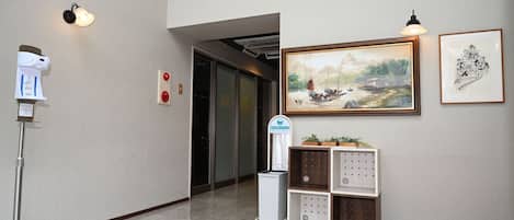 A hallway with a water dispenser, a fire alarm, a framed painting, and a small plant display.