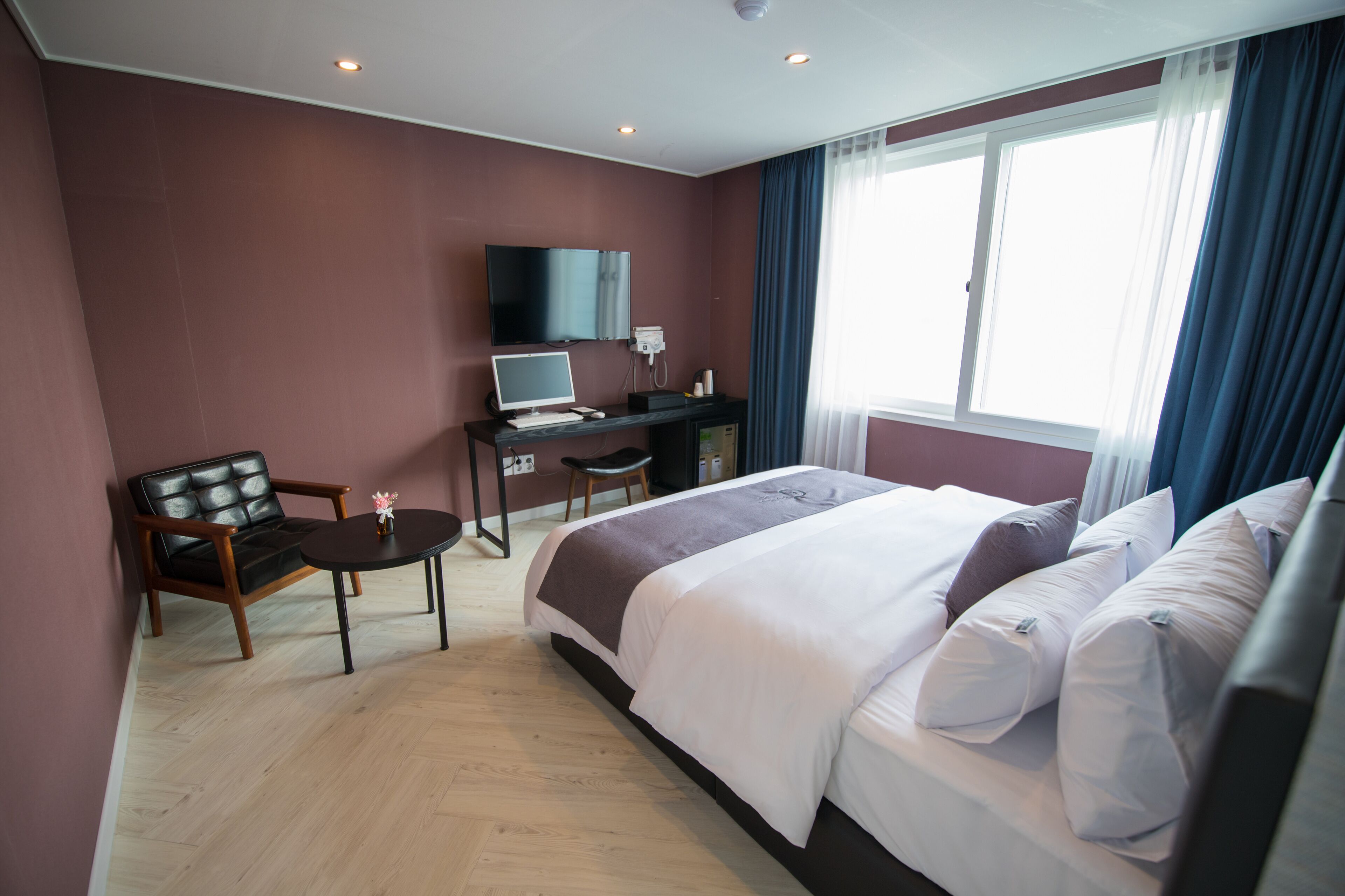 Habitación de hotel con cama, escritorio, silla, televisor y ventana con cortinas.