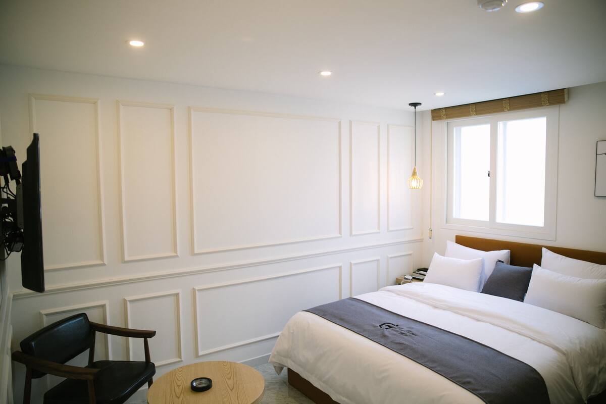 A hotel room with a bed, a chair, a small round table, and a wall-mounted TV.