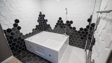 A modern bathroom with a large white bathtub, black and white hexagonal tile walls, and a wooden floor.