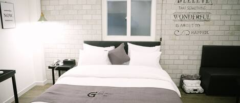 Habitación de hotel ordenada con una cama, una mesita de noche, una lámpara, un ventanal y una frase motivadora en la pared.