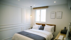 A hotel room with a large bed, a desk with a computer, and a window with two wall art pieces. - Gray Boutique hotel (Tongyeong)