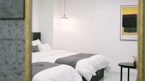 Ein modernes Schlafzimmer mit einem großen Spiegel, einem Bett mit weißer und grauer Bettwäsche, einem kleinen Nachttisch und einer hängenden Leuchte.