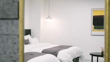 Quarto moderno com um espelho grande, cama com roupa de cama branca e cinza, mesa de cabeceira pequena e luminária pendente.