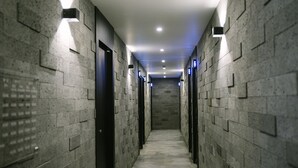 A narrow hallway with a tiled floor and walls, illuminated by recessed ceiling lights and wall-mounted fixtures. - Gray Boutique hotel (Tongyeong)