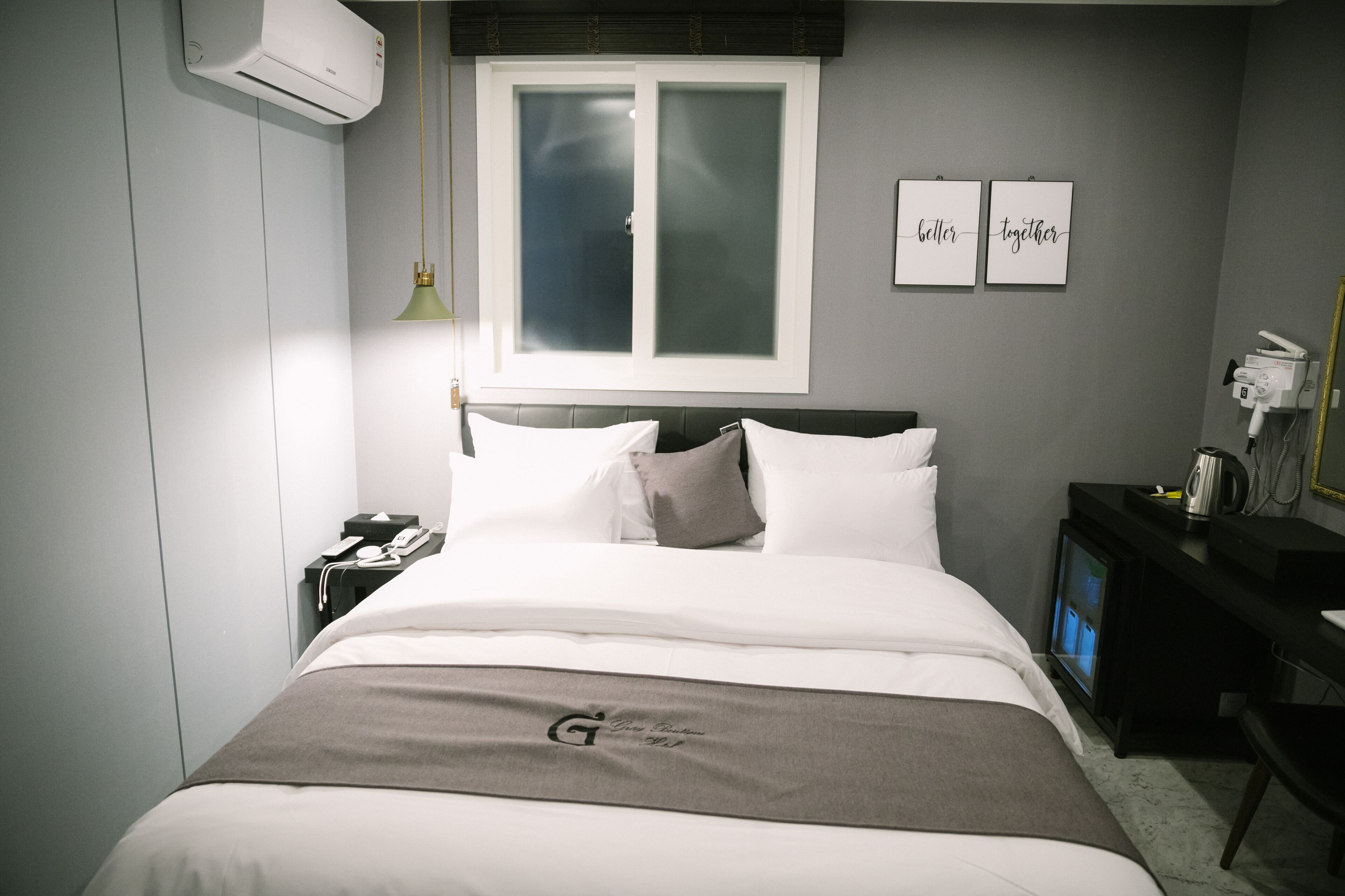 A hotel room with a bed, a nightstand, a desk, a TV, and a window with frosted glass.