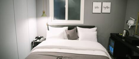 A hotel room with a bed, a nightstand, a desk, a TV, and a window with frosted glass.
