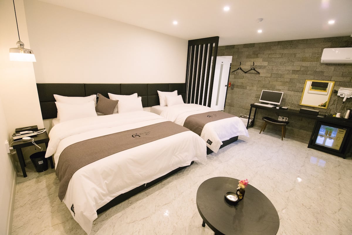 A hotel room with two beds, a desk with a computer, a TV, and a small table with a vase.