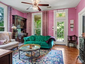 A room with a green sofa, a patterned armchair, a glass coffee table, and a wooden cabinet.