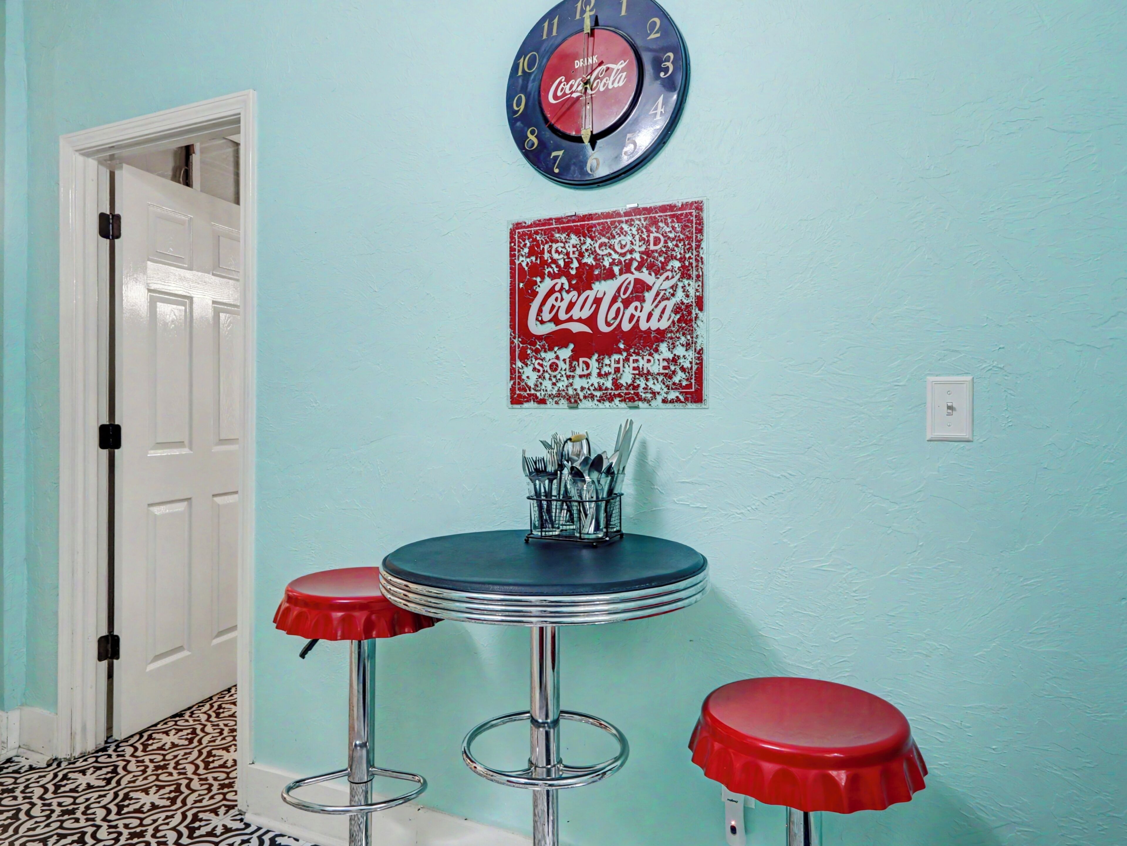 A room with a Coca-Cola clock, a vintage Coca-Cola sign, and two red bar stools.