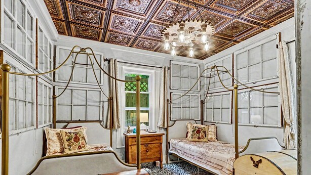 A room with a wooden bed, a wooden chest, a small table, and a chandelier. - Walk to Bathhouse Row! Queen Anne Victorian Cottage (Hot Springs)