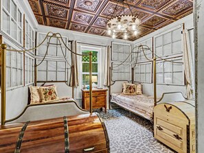 A room with a wooden bed, a wooden chest, a small table, and a chandelier.