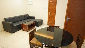 A living room with a sectional sofa, a glass-top dining table, and wooden chairs. - Ncomforts Stay inn (Tbilisi)